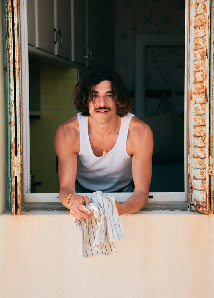 GIOVANNI ZATTERA à la fenêtre portant un débardeur blanc et les bijoux de la capsule ALHAJA