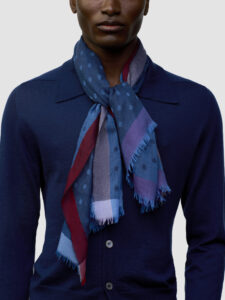 Gros plan sur le foulard ultraléger Wispy à pois et rayures rouges:bleues:violettes noué, sur un cardigan fin bleu marine, Begg x Co, Vanessa Seward