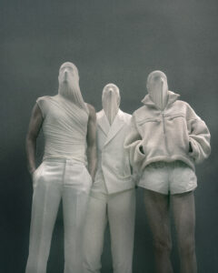 Trois silhouette LGN FW26 en costume blanc avec headpiece sombre évoquant l’esthétique Alien.