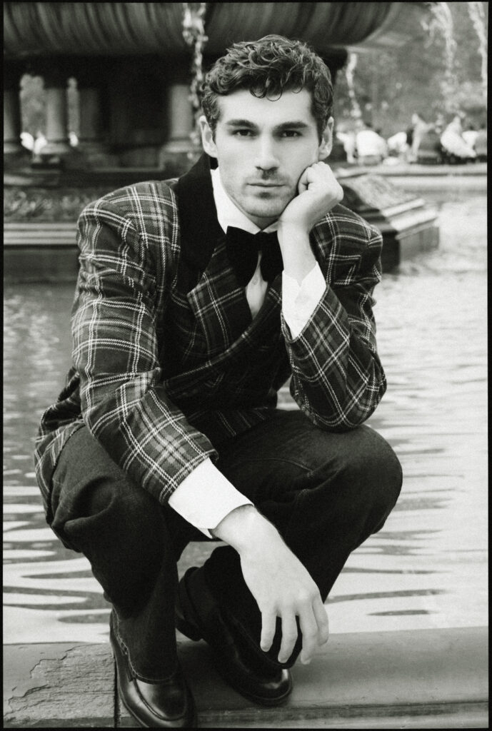 Portrait éditorial masculin en noir et blanc photographié à New York par Elys Berroteran, hommage à Ralph Lauren, avec Anselmo Menéndez devant une fontaine à Central Park dans un tailoring à carreaux élégant.
