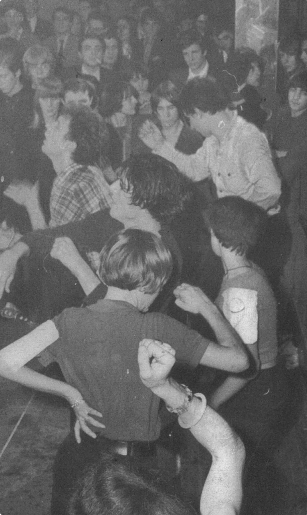 Crowded dance floor with people dancing closely and raising arms at a party (black and white).