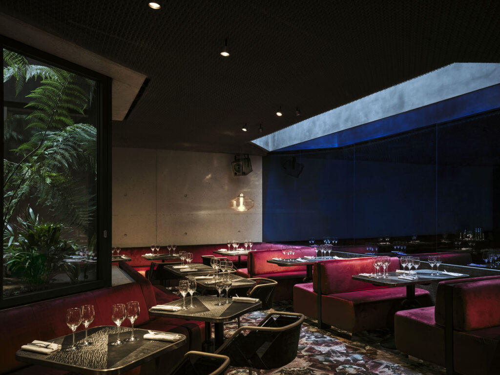 Dimly lit restaurant dining area with red velvet booths, black tables, and wine glasses set for service.