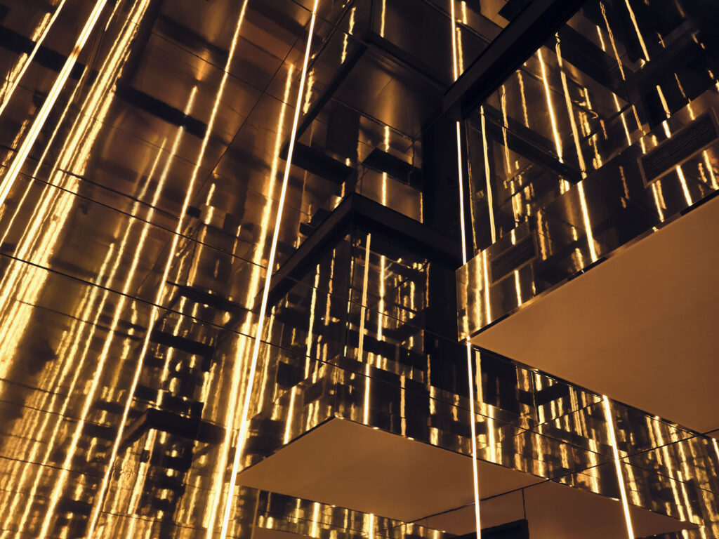 Abstract interior with glowing vertical amber light strips along mirrored panels and angular architecture.