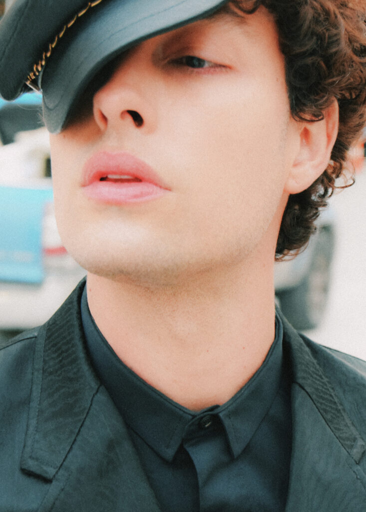 Close-up portrait of a young man wearing a dark green cap tilted over his eyes, lips slightly parted.