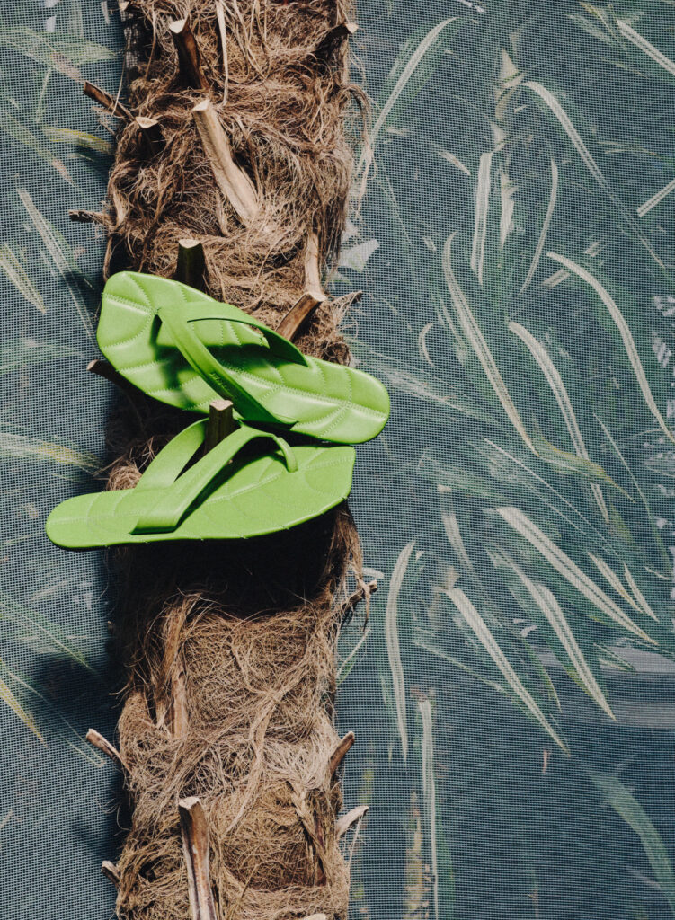 Bright green quilted sandals resting on a rough, hairy tree trunk with a mesh-patterned background.