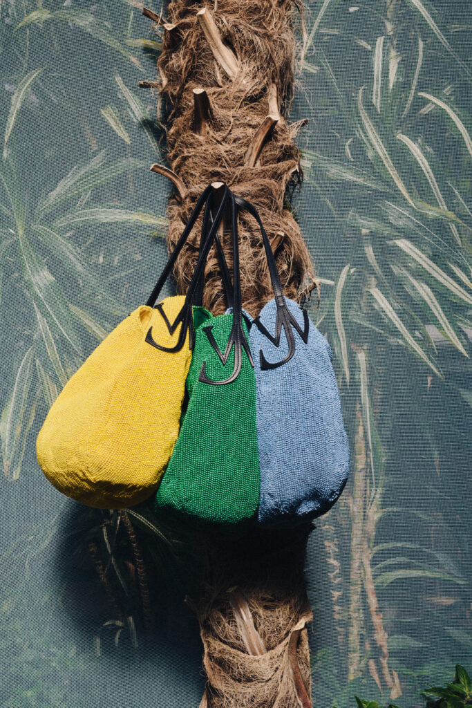 Coarse rope wrapped around a tree trunk with three colorful towels—yellow, green, and blue—hanging from it in front of a mesh background.