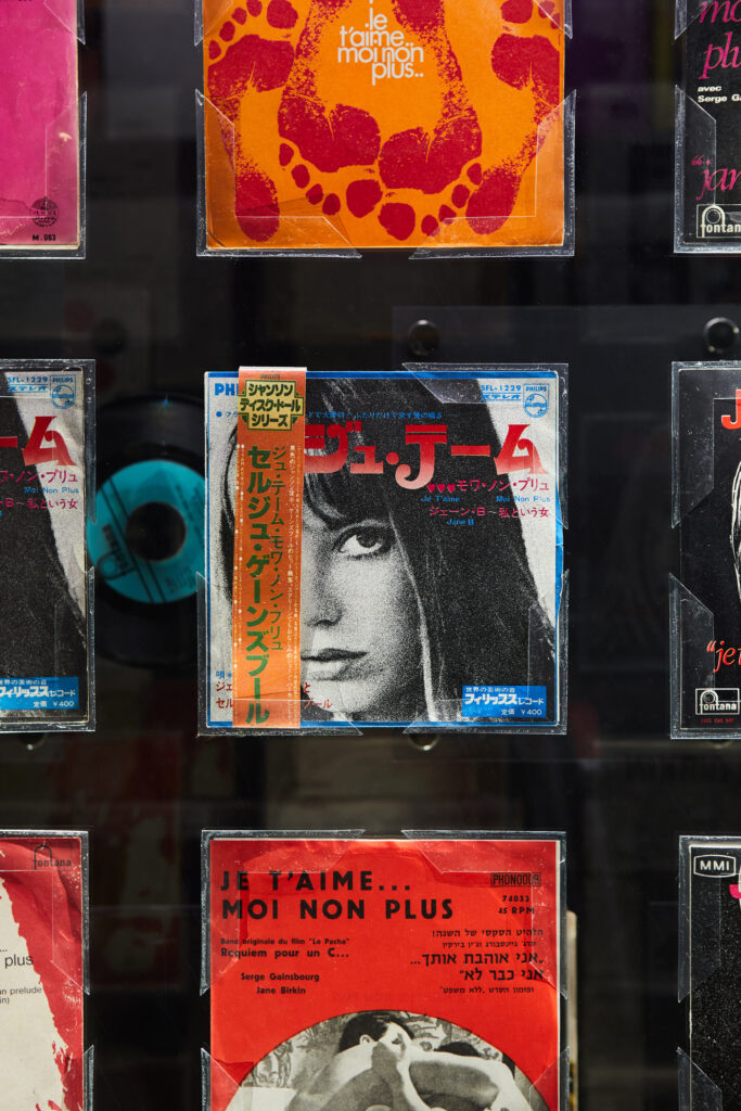 Assorted vintage movie posters in a glass display, featuring an orange circular design at center and a black-and-white portrait with blue borders toward the bottom.