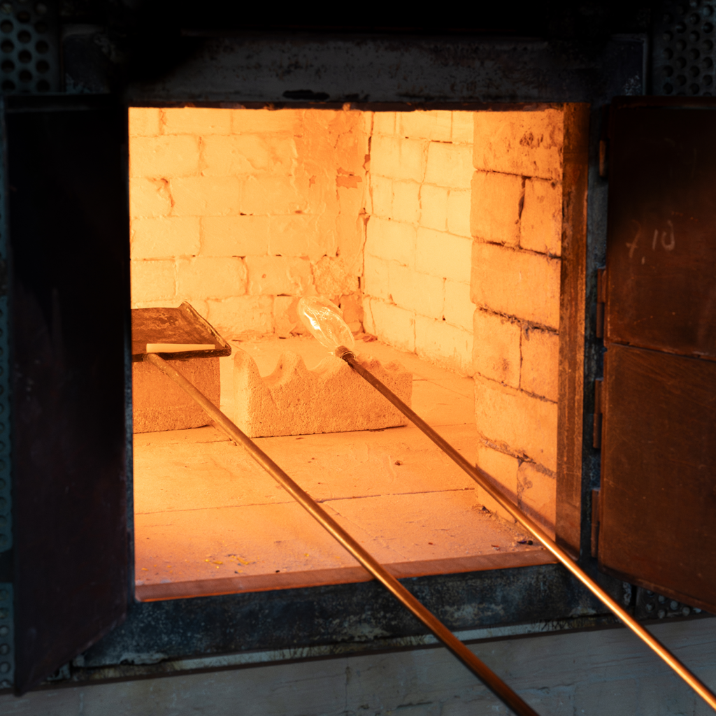 Orange-hot interior of a brick kiln with a glass rod being heated by long metal tongs