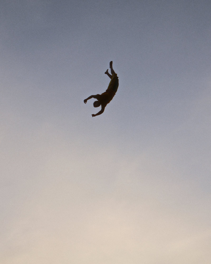 Silhouette of a person performing a backflip high in the sky against a pale blue gradient.