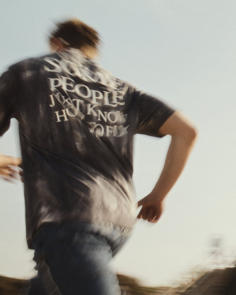 Back view of a person running outdoors, wearing a dark T-shirt with white text on the back (motion blur).