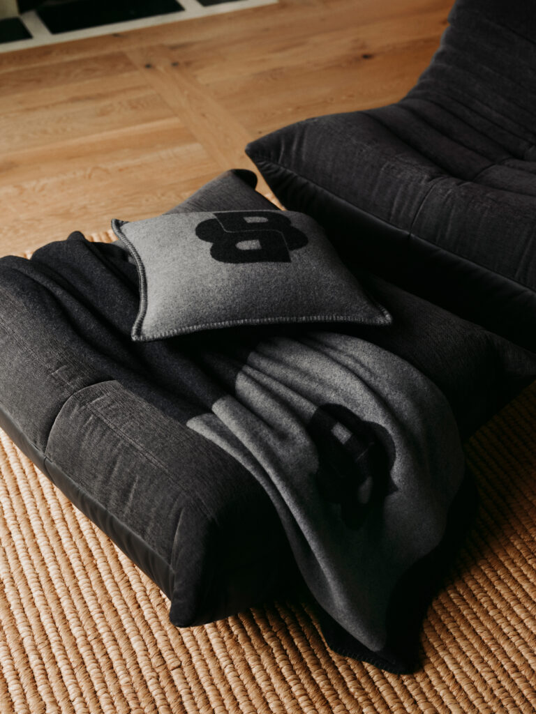 Close-up of dark gray sofa cushions on a beige woven rug with a gray throw pillow featuring a bold black number.