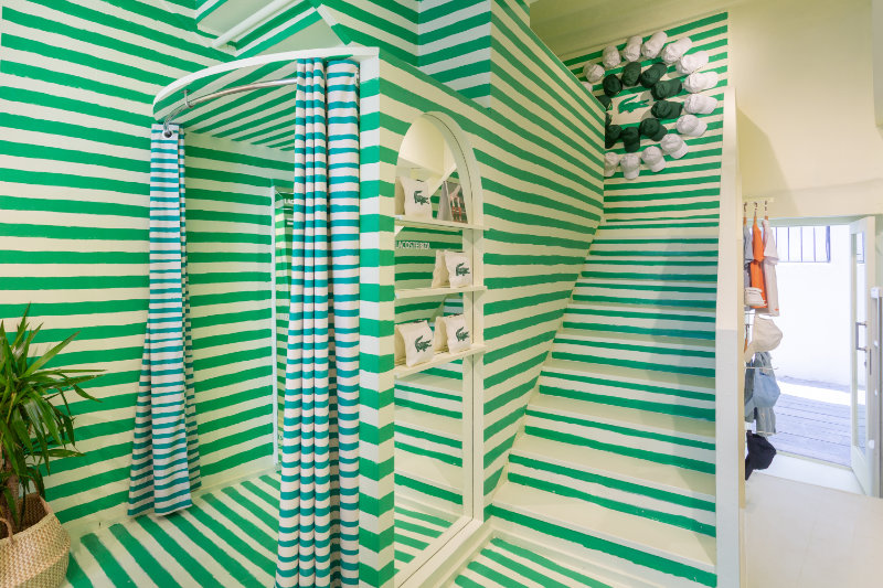 Boutique change area with green-and-white striped walls, striped curtain and shelves displaying bags or apparel.