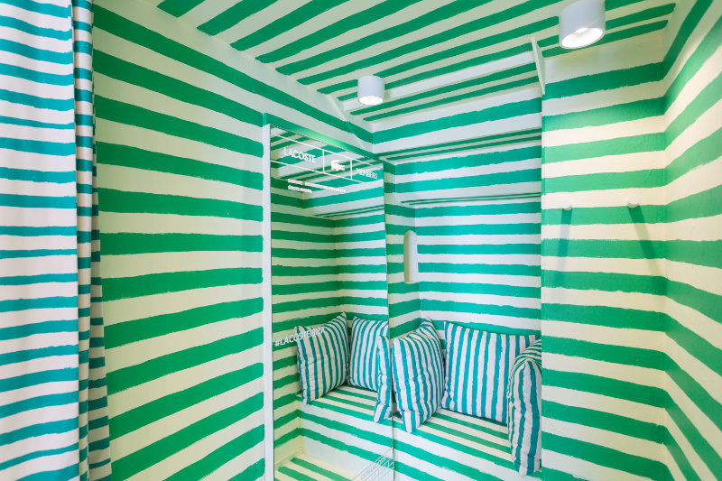 Room with bold green and white horizontal stripes, built-in booth seating with blue-and-white striped cushions and ceiling lights.