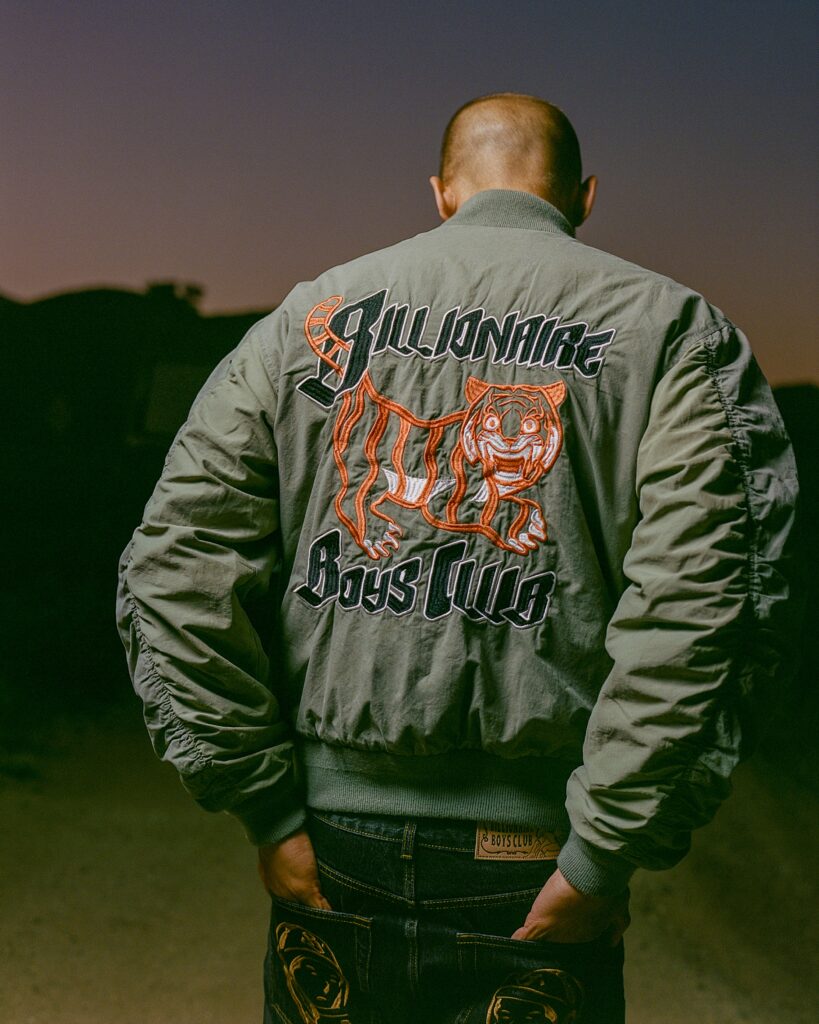 Back view of a person wearing a green bomber jacket with orange tiger embroidery, standing at dusk.