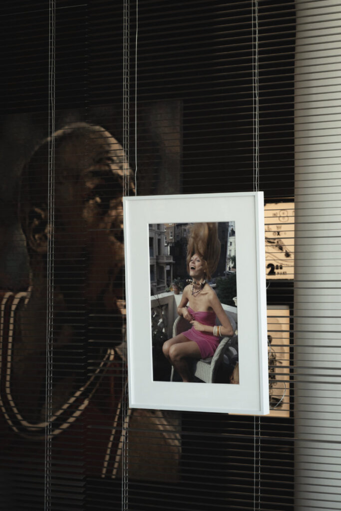 Framed photograph of a laughing woman in a pink dress, hanging in front of window blinds.