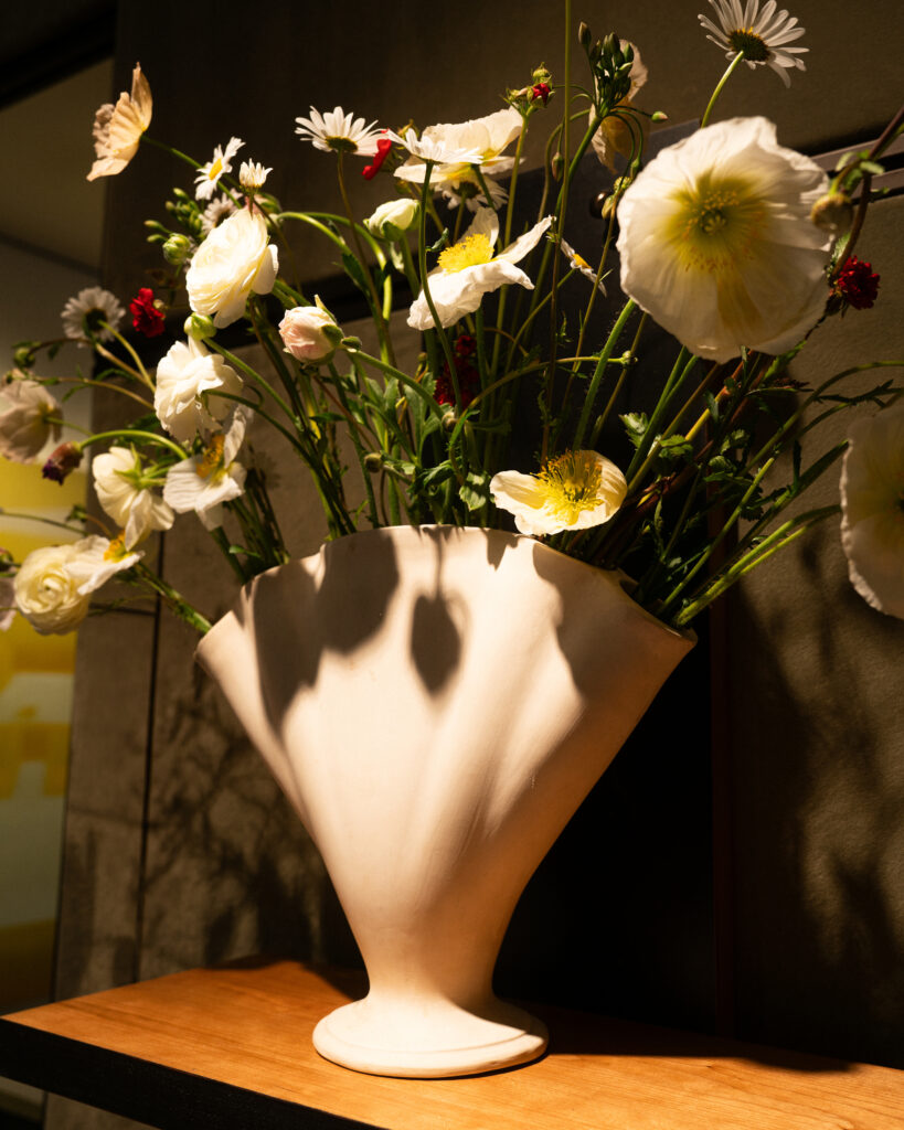 White bouquet of white flowers with yellow centers in a pale paper wrap on a wooden surface against a dark background.
