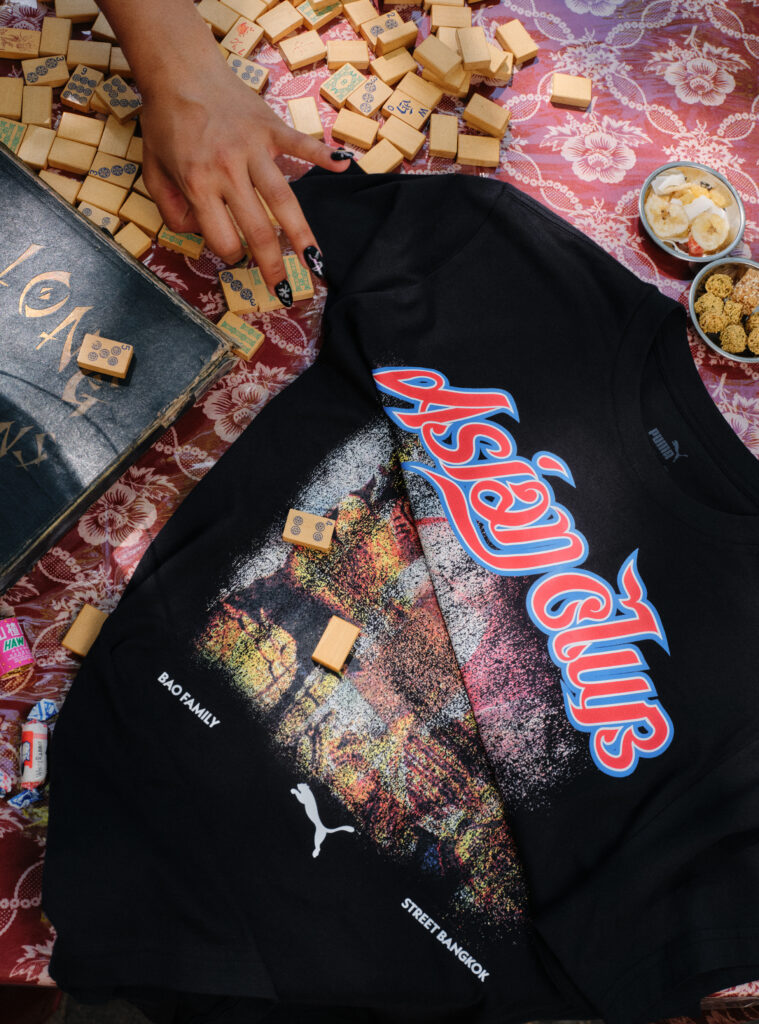 A hand among many small wooden blocks with blue symbols on a red patterned cloth, next to a black graphic T‑shirt and bowls of snacks nearby.