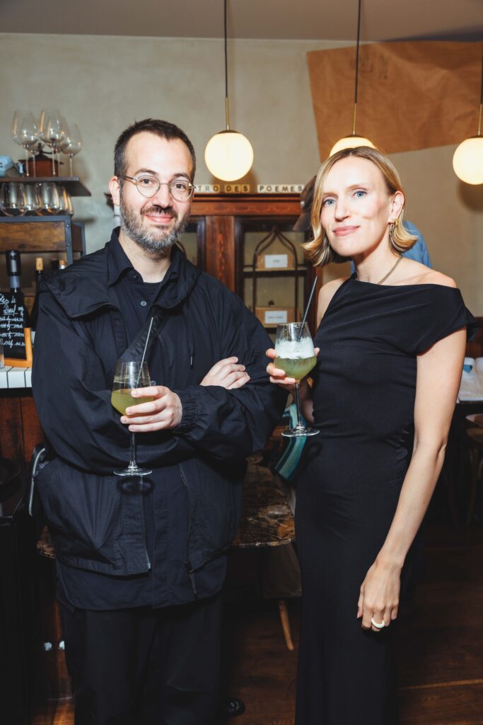 Two adults in a dim bar, each holding a stemmed cocktail, smiling at the camera.