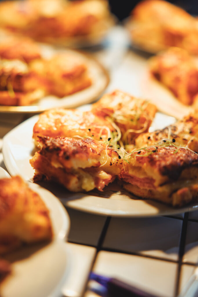 Blurry close-up of golden-brown mini pizzas on white plates, topped with cheese and herbs.