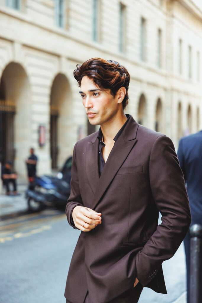 Young man in a brown suit walking along a city street, looking to the side.