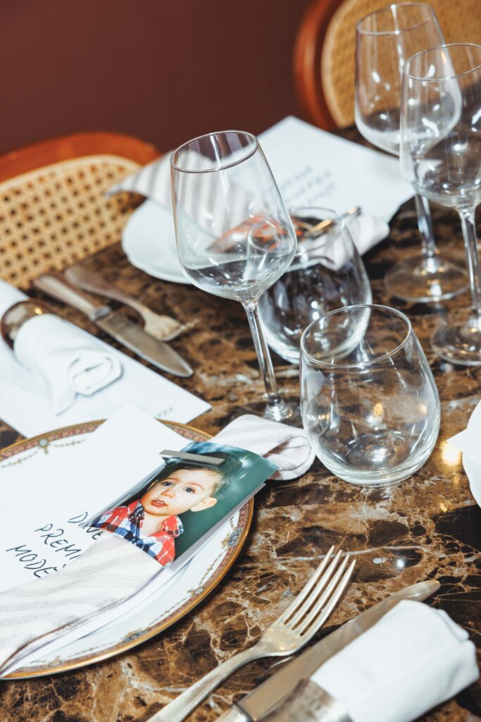 Close-up of a formal dining table with wine glasses, cutlery, a rolled napkin, and a photo card on a marble table surface