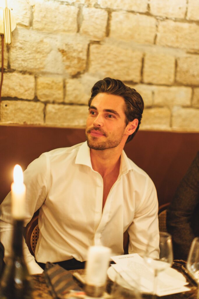 Man in a white shirt seated at a candlelit table, with a brick wall behind.