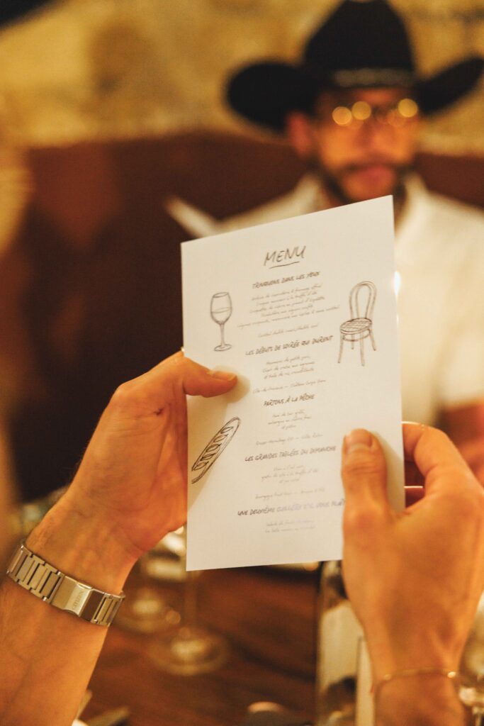Person in a black cowboy hat holds a small menu card up to the camera.