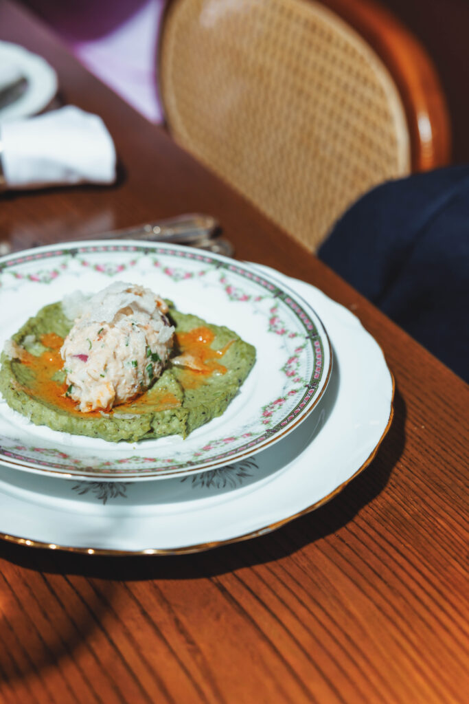 Plate with a green, flat-round spread topped with a scoop of tuna salad on a decorative china plate, set on a wooden table