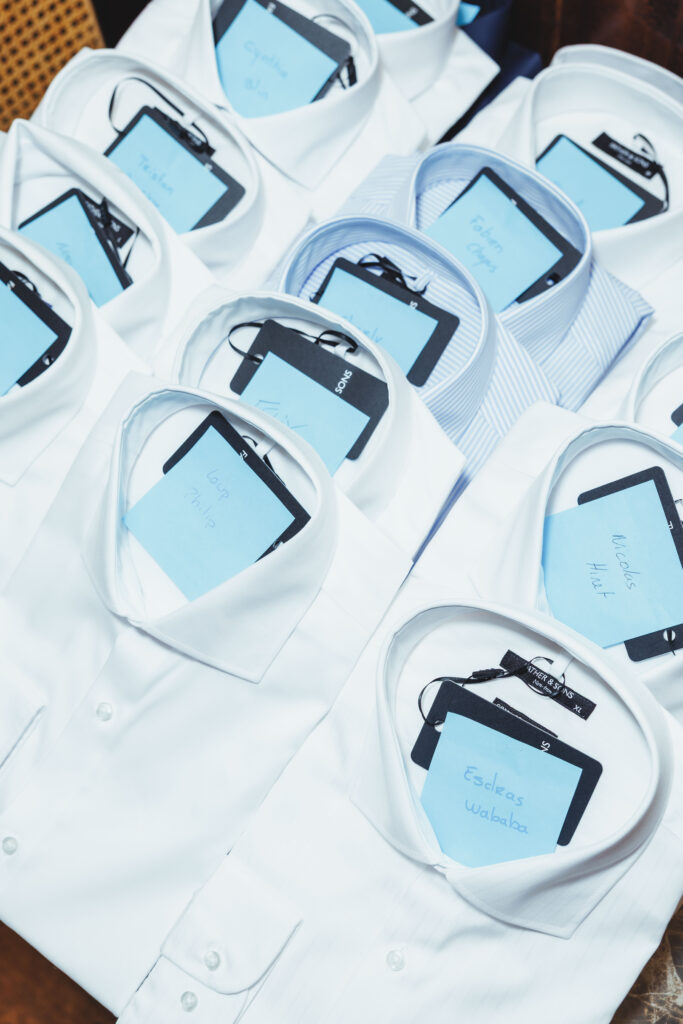 Pile of white dress shirts with blue name tags tucked in pockets, arranged in a scattered display.