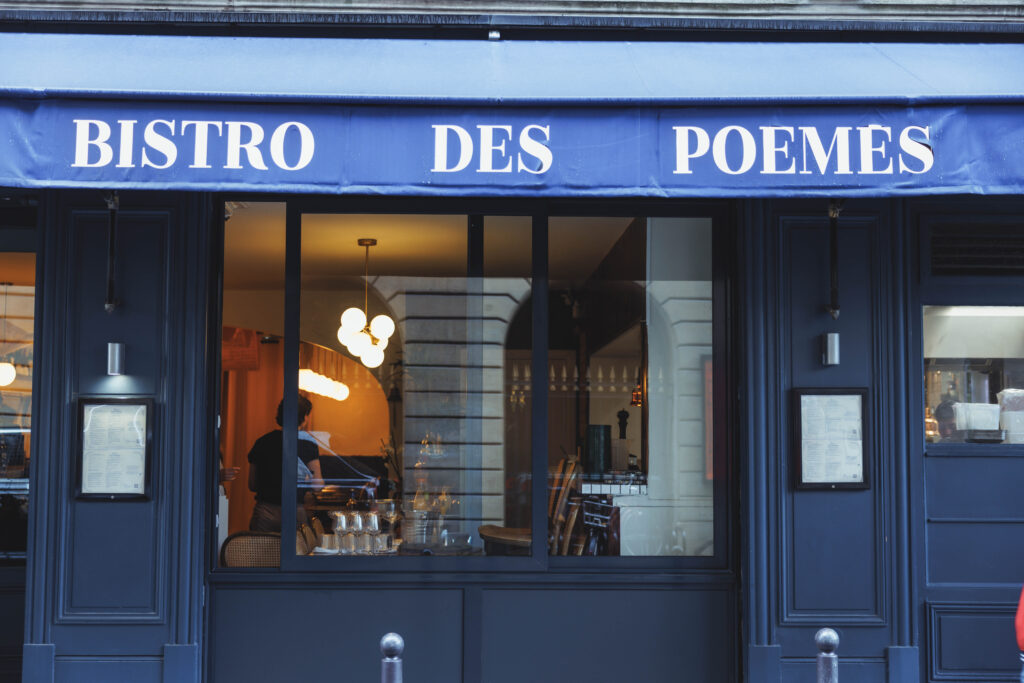 Blue storefront with the sign 'BISTRO DES POEMES' and warm interior lighting visible through the windows.