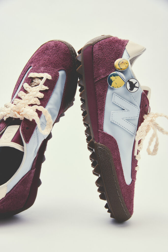 Pair of burgundy suede sneakers with light blue panels, cream laces, and chunky brown soles photographed from the side. A few decorative pins are attached to the side.