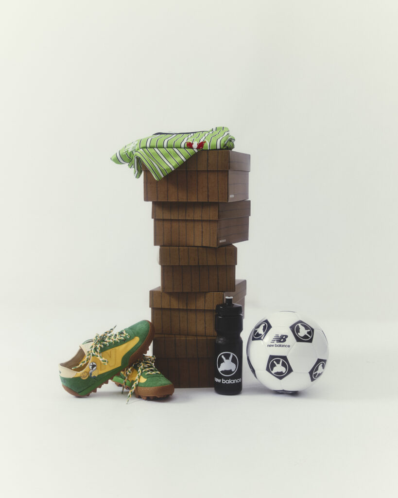 Stack of brown wooden boxes with a folded green striped shirt on top; a soccer ball and water bottle sit at the base, with green-yellow sneakers nearby.
