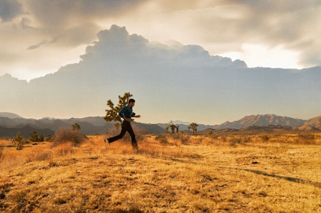 Joseph Reuben runs across a dry, sunlit desert with mountains in the distance during golden hour.