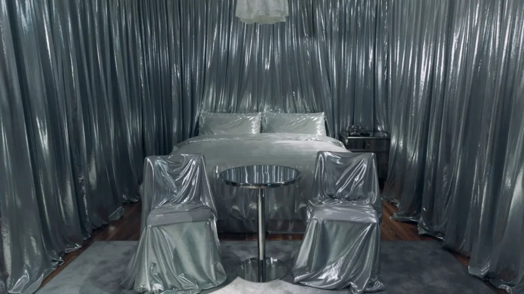 Bedroom fully wrapped in silver plastic sheeting, including bed, chairs, and furniture found in the room.