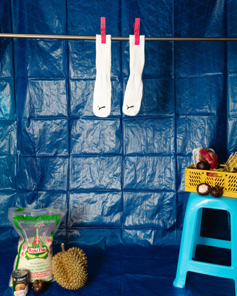 White socks hanging on a clothesline with pink clothespins against a blue tarp, with groceries nearby and a blue chair in view.