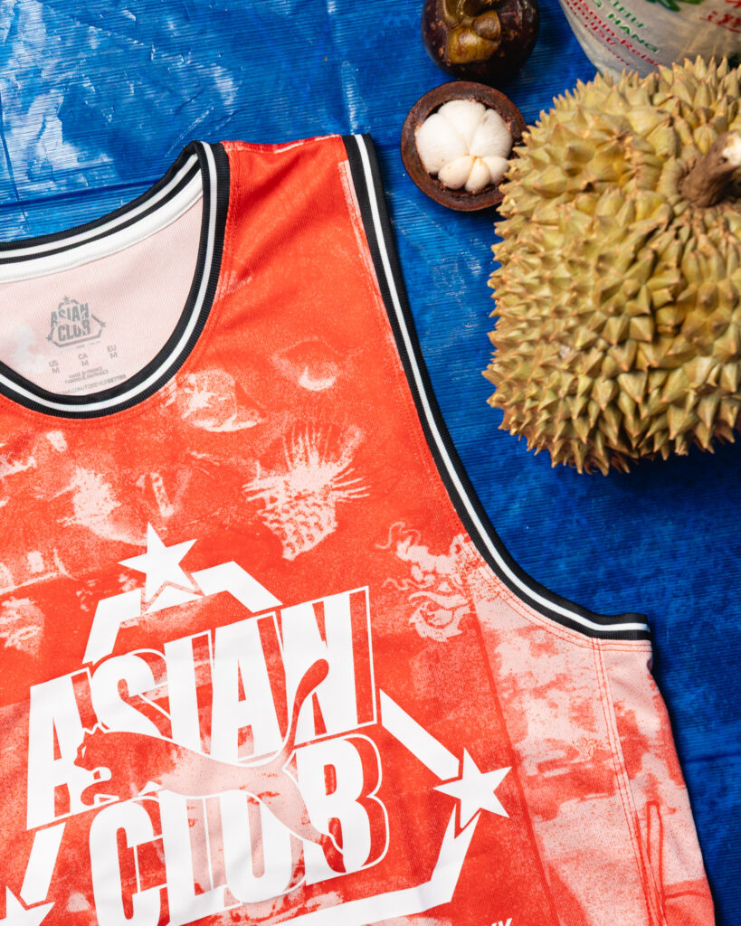 Close-up of an orange basketball jersey on a blue wooden surface, with a durian fruit to the right.