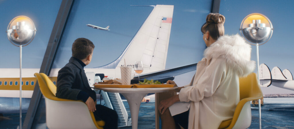 Woman and child dining at a table, with airplane mural and ocean backdrop in a themed restaurant or exhibit space.
