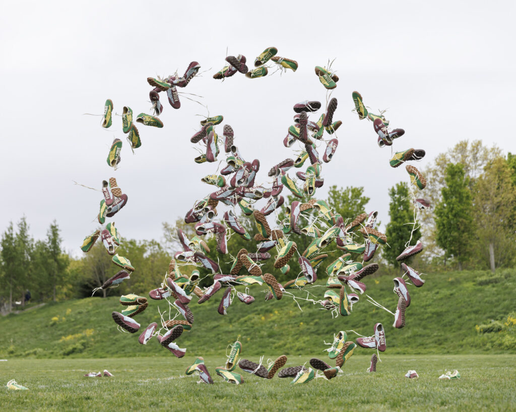 Colorful sneakers tied to strings fly upward in a park as part of an outdoor shoe installation art piece.