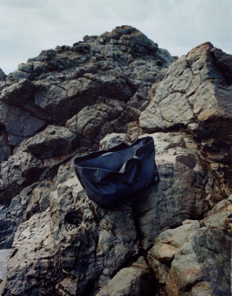 Rugged gray rocks with a dark bag resting on the uneven surface near a rocky shoreline.