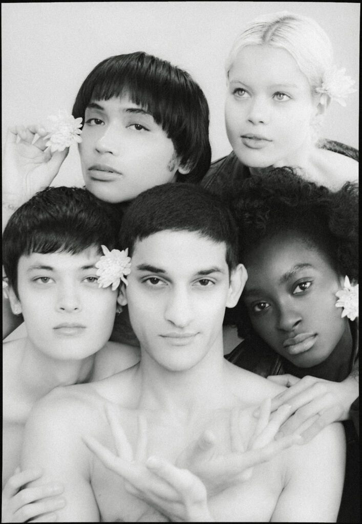 Black-and-white group portrait of six young people with flowers in their hair, posed closely together.