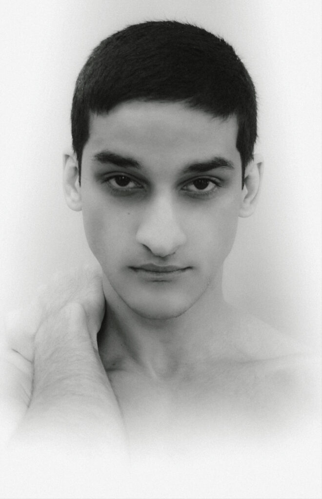 Close-up black-and-white portrait of a young man with short dark hair, hand resting on his neck.