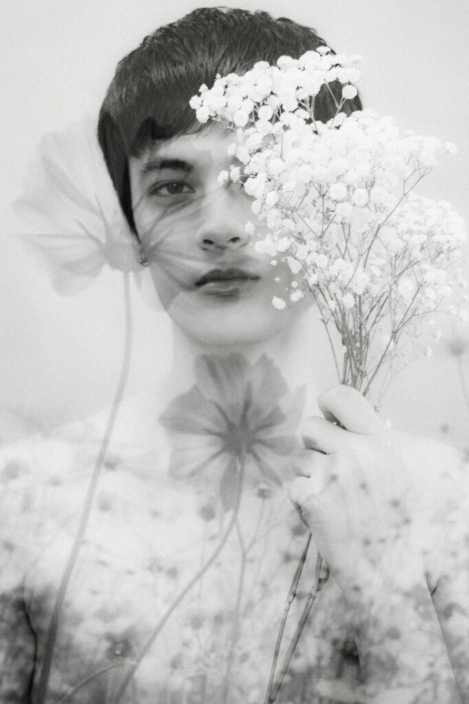 Black-and-white portrait of a young person, with a bouquet of baby's breath held near the face in a soft double-exposure effect.