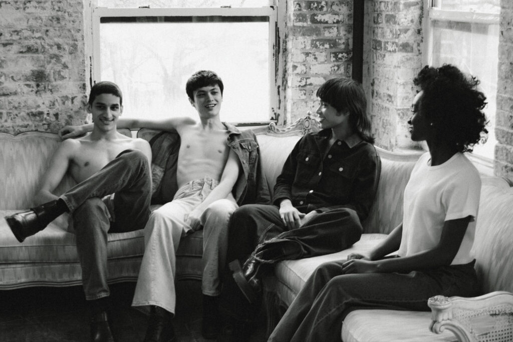 Four friends relaxing on a vintage sofa in a brick-walled room, smiling and talking together.