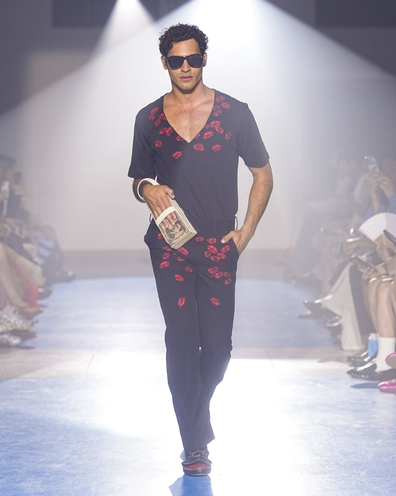 Silhouette doublet SS27 portant un ensemble noir marqué de traces de rouge à lèvres, avec lunettes noires et pochette à la main.